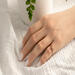 Hand wearing 14K yellow gold birthstone stackable rings with 2mm round stones sizes 4-10 on a white fabric with green plant in background  
